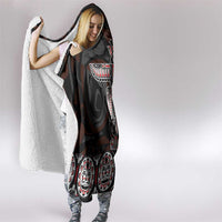 Hooded blanket with dark print, sherpa-lined hood, and totem design on front