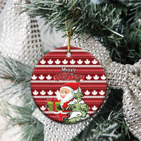 Red round ceramic Christmas ornament hanging on tree; Santa scene and Merry Christmas over maple leaf pattern.