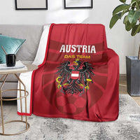 Red Austria football blanket with team emblem, laid over gray sofa seat