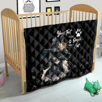 Black quilt blanket on a wooden crib, with gray cat graphic and paw print text