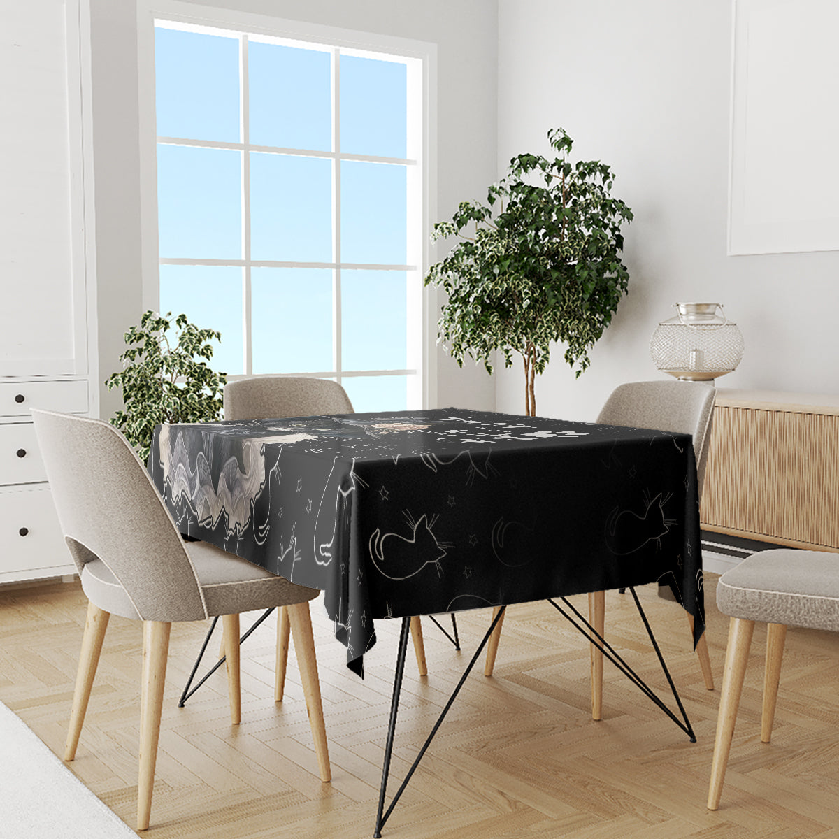 Black cat-themed tablecloth on dining table with four light-colored chairs