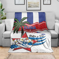 White blanket on gray couch with blue/red stripe design, palm tree, bird, and “Patria y Vida”