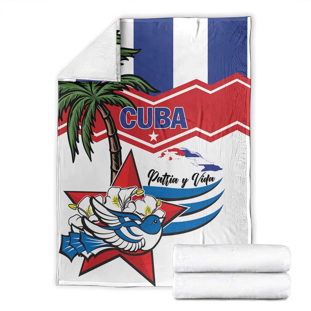 Folded white blanket with blue/red design, palm tree, blue bird, and “Patria y Vida”