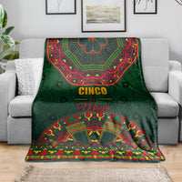 Green Mexican folk blanket with 'Cinco de Mayo' center print, on gray sofa