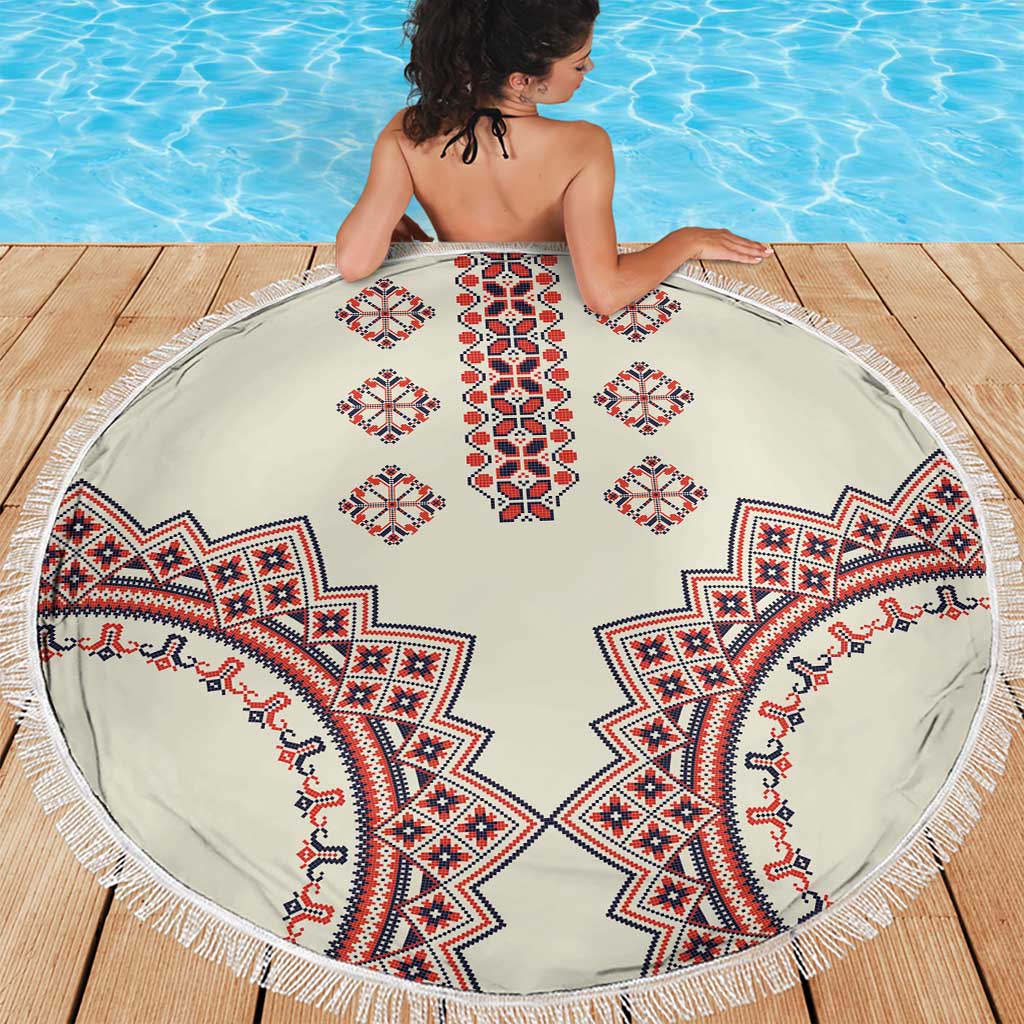 Round beige beach blanket with fringe, red and blue traditional motifs, on a wooden deck