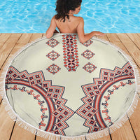 Round beige beach blanket with fringe, red and blue traditional motifs, on a wooden deck