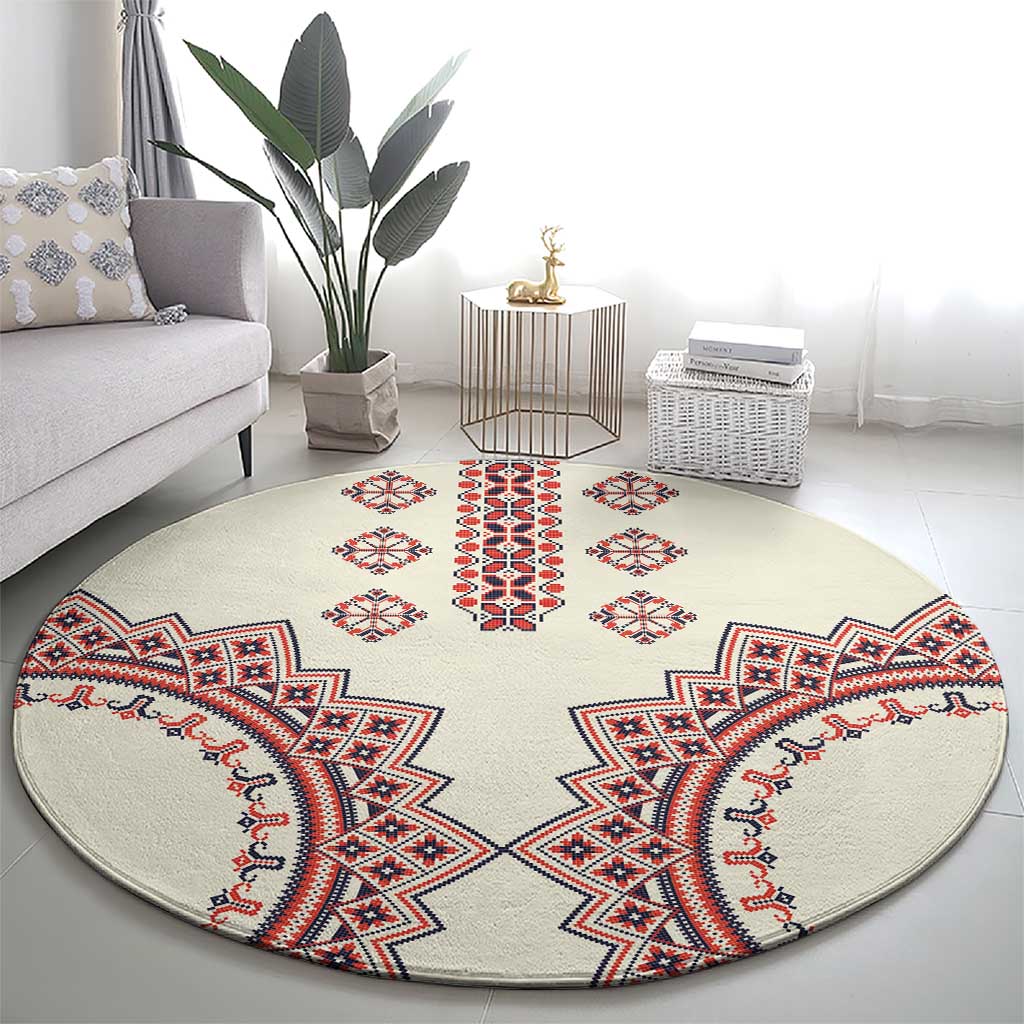 Beige round rug with symmetric geometric embroidery in red, blue, and white, wide view