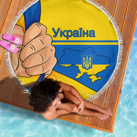 Round beach blanket with Ukraine flag graphic, comic fist and trident, laid on wood floor