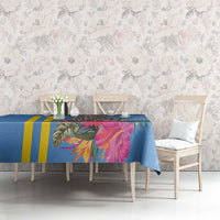 Blue tropical tablecloth with pink flowers, green tropical leaves, and yellow stripe