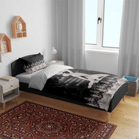 Bedding set on bed: black duvet cover with silver floral border, seated figure print, two pillows