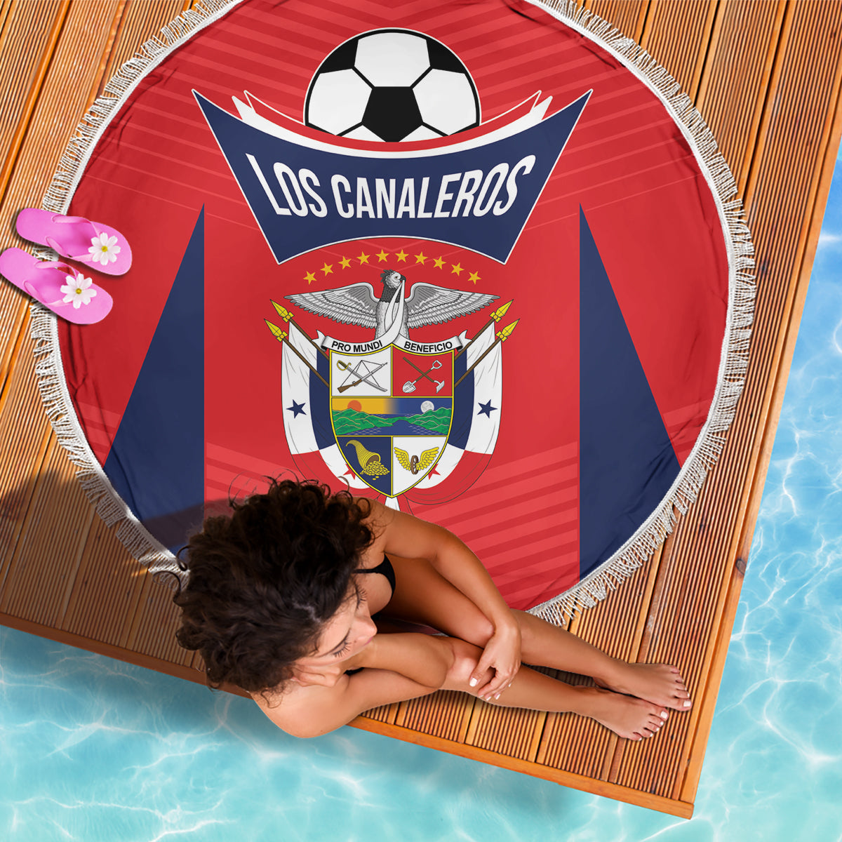 Red round fringe football beach blanket with Los Canaleros crest, lying on pool rug