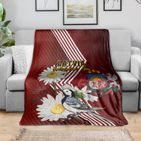 Red blanket on sofa with Latvia text, crest, wagtail bird, and daisy flowers