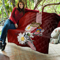 Red quilt draped over sofa with Latvian diagonal stripes, daisies, crest and bird art