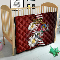 Red quilt in crib with Latvian diagonal stripes, daisy flowers, crest emblem, and bird