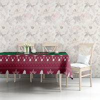 Christmas tablecloth on table with maroon geometric pattern, green strip, white pine trees and snowflakes
