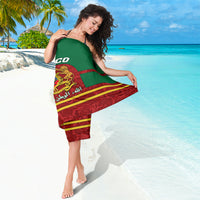 Green Morocco sarong tied on shoulder, crest emblem and red striped bottom