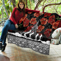 Black quilt held outdoors, showing red poppies, white monument design, and decorative Polynesian border