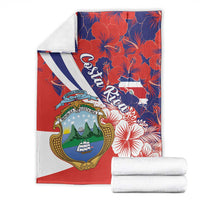 Folded red blanket featuring Costa Rica coat of arms, hibiscus pattern, and white-blue diagonal
