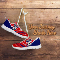 Red and blue soccer sneakers with white sole and white laces, angled on wood