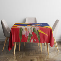 Red tablecloth with large pink flowers and green leaves over rectangular dining table