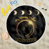 Black round beach blanket with white fringe, crescent eclipse graphic, “From the Universe” text