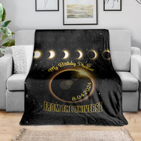 Black eclipse-themed throw blanket on sofa with gold crescent rings and “From the Universe”