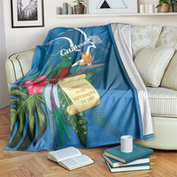 Blue tropical throw blanket draped on sofa with quetzal, flowers, and Guatemala banner