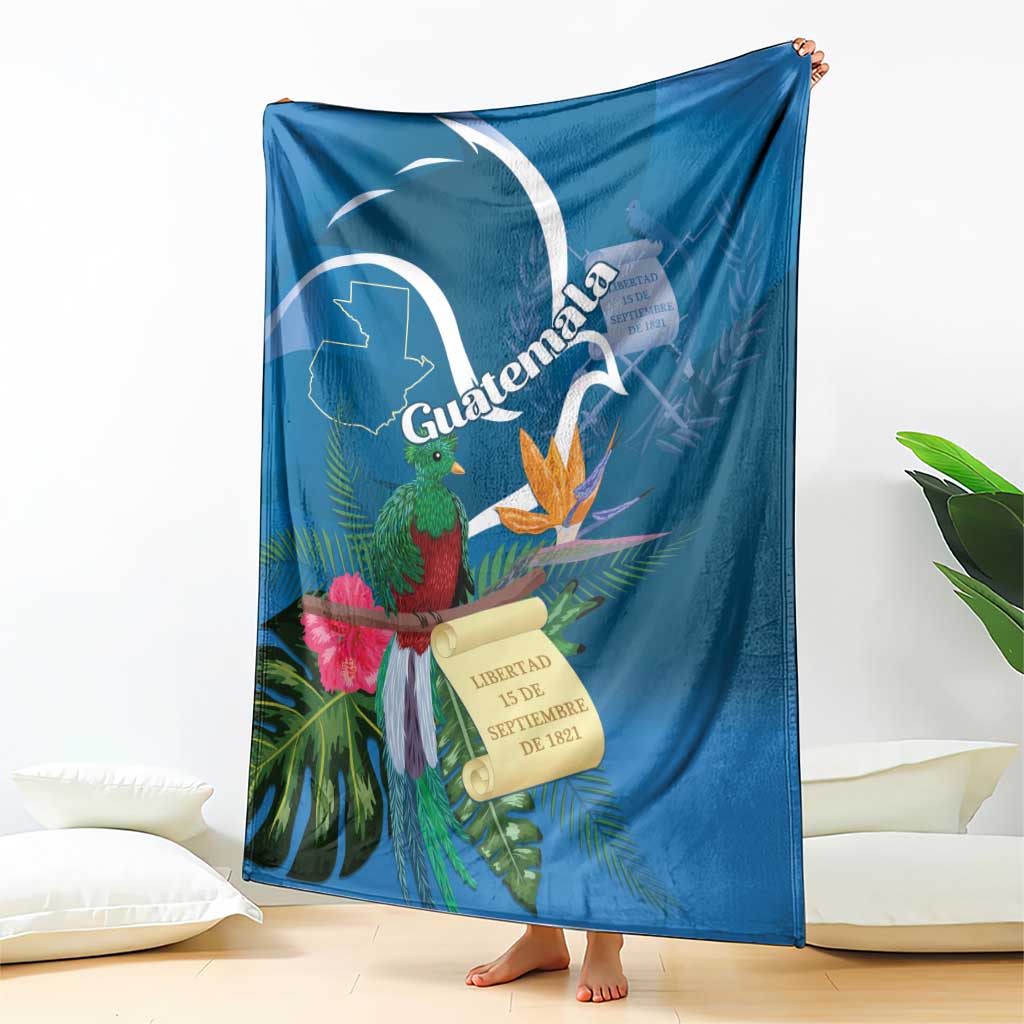Blue tropical throw blanket hanging on bed with quetzal, flowers, and Guatemala banner