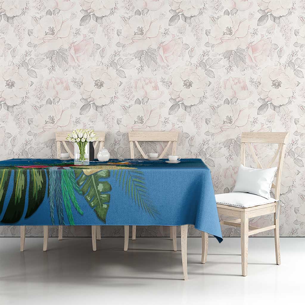 Blue tropical tablecloth with green leaf print, spread across a table behind white chairs.