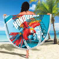 Round blue beach blanket with macaw design and white fringe, held up on the sand