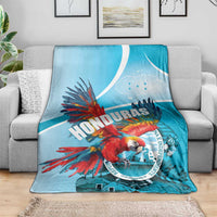 Sky blue throw blanket with red macaw artwork and Honduras text inside circular emblem.