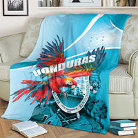 Sky blue throw blanket draped over sofa with red macaw print and Honduras graphic in circle.
