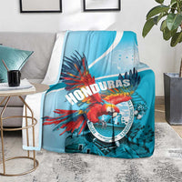 Sky blue Honduras throw blanket on floor with red macaw artwork and circular emblem design.