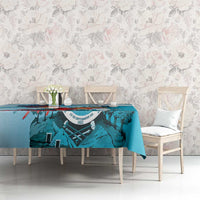 Teal-blue printed tablecloth with crest and colorful bird illustration along top edge