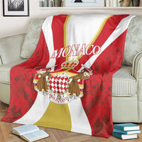 Red, white, and gold Monaco crest blanket draped on a sofa