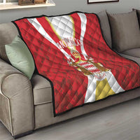Red Monaco quilt laid on a gray sofa, with white-gold stripe and centered crest emblem