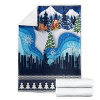 Folded blue Christmas blanket with Santa sleigh over snowy skyline and pine tree border.