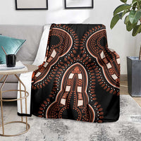 Black dashiki pattern blanket with ornate orange figure motif, laid over sofa