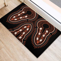 Black rubber doormat with orange and white tribal elephant silhouettes, angled view on wood.