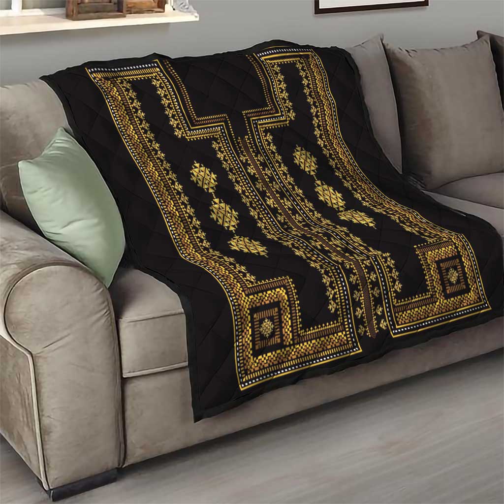 Black quilt throw with gold ornamental borders and diamond patterns, folded over a sofa.