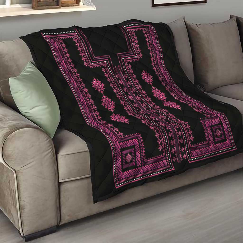Black quilt blanket with pink border and repeating diamond medallions on sofa.