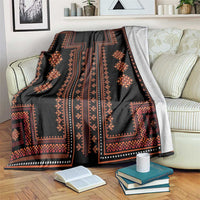 Black traditional geometric blanket with orange-red motifs and blue border, draped on a sofa