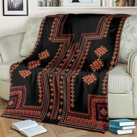 Black traditional pattern blanket with orange diamond motifs and blue stripe border on a couch