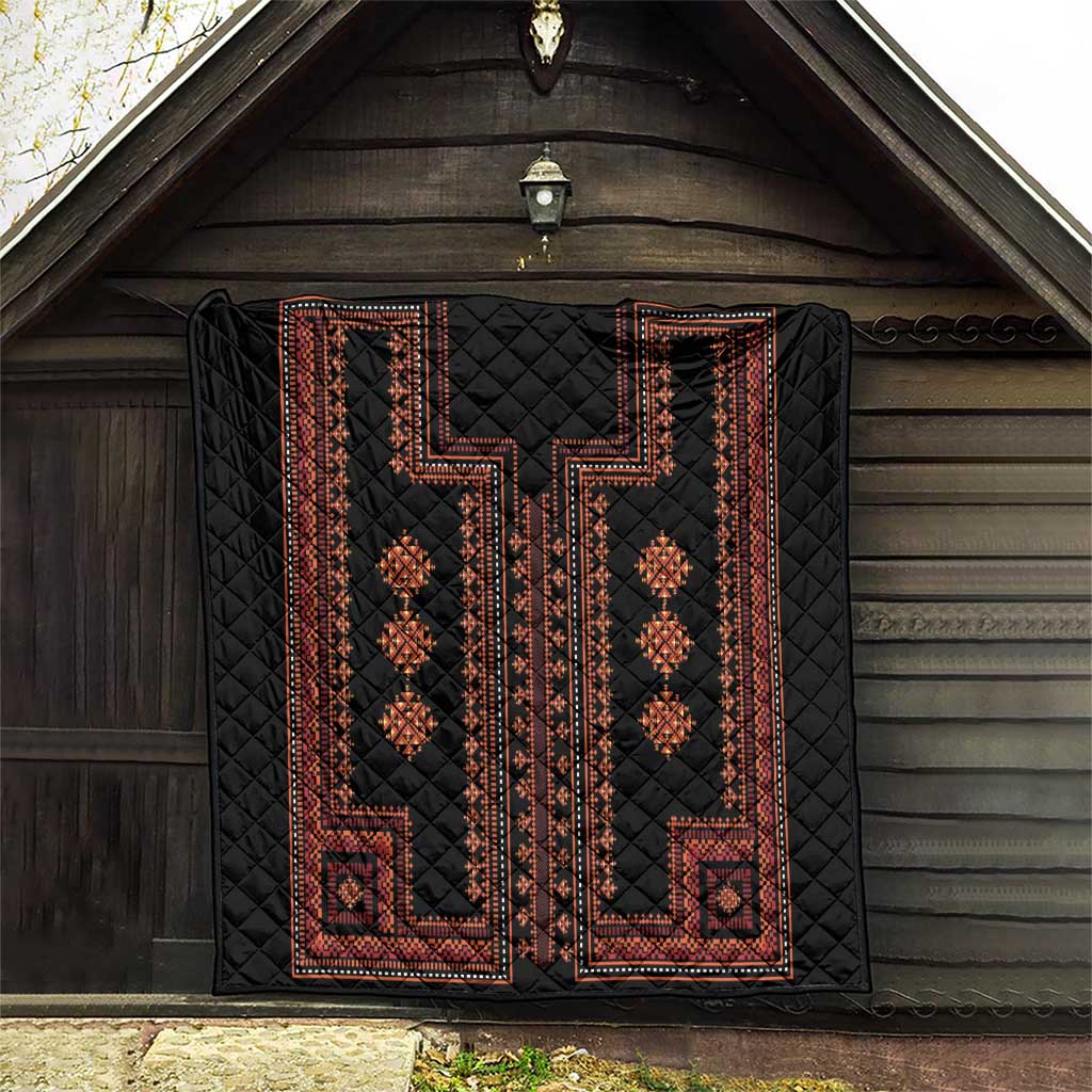 Black quilt with red geometric border and diamond motif panels displayed in a barn.