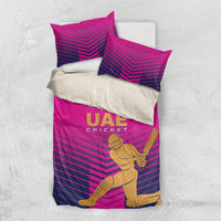 Pink UAE cricket bedding set laid flat, chevron stripes with gold logo and player graphic