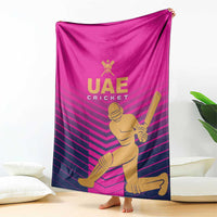Pink UAE Cricket blanket featuring gold batsman graphic and purple striped design, draped on floor