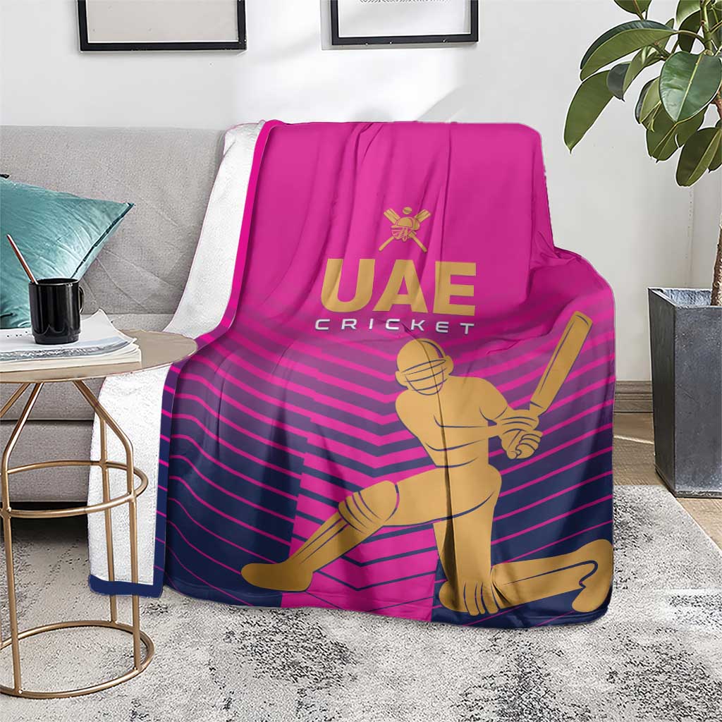 Pink UAE Cricket blanket with gold batsman graphic and purple chevron stripes, laid on chair/bench