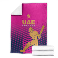 Pink UAE Cricket blanket with gold batsman graphic and dark striped pattern, folded with rolled towels