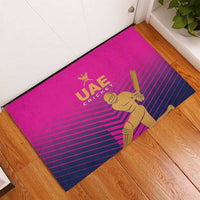 Pink UAE Cricket doormat on floor, showing gold batter and UAE Cricket logo with stripes