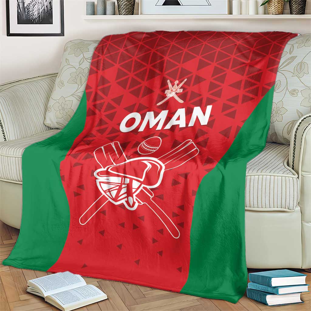Red and green Oman cricket blanket on a couch with white “OMAN” and helmet illustration
